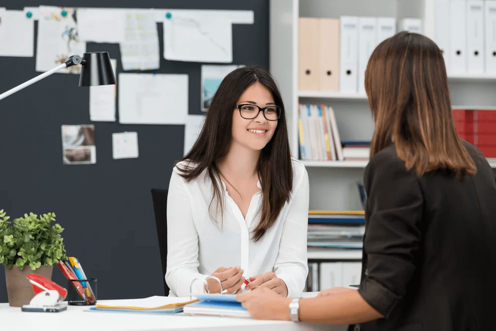 Two young businesswomen having a meeting in the office sitting at a desk having a discussion with focus to a young woman wearing glasses (1)